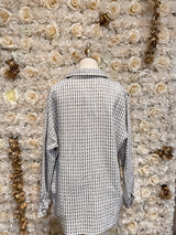 Mannequin wearing a white checkered oversized tweed shacket with a pink bra underneath, displayed in a floral-themed setting.