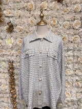 Mannequin wearing a white checkered oversized tweed shacket with a pink bra underneath, displayed in a floral-themed setting.