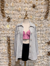 Mannequin wearing a white checkered oversized tweed shacket with a pink bra underneath, displayed in a floral-themed setting.