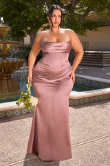 A woman modeling a floor-length strapless satin bridesmaid dress in dusty rose pink, standing outdoors in front of a fountain and tiled pool area.