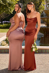 Two women modeling floor-length strapless bridesmaid dresses outdoors beside a fountain. The woman on the left wears a dusty mauve satin gown and faces away, while the woman on the right wears a rust-brown satin gown and faces forward, holding white flowers.