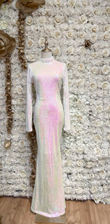 A white backless maxi dress with sequin open back, displayed on a mannequin against a floral wall backdrop.