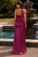 A woman stands outdoors in front of a fountain and tiled pool, wearing a sleeveless magenta formal gown with an open back and draped neckline. The photo is taken from behind to show the back of the dress.
