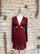 Burgundy sequin mini dress with cutouts and puff sleeves, displayed on a mannequin against a floral backdrop.