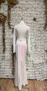 A white backless maxi dress with sequin open back, displayed on a mannequin against a floral wall backdrop.