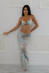 halter-style silhouette features a ruched bust with a center twist detail, cascading into a low-rise waist and sultry open sides wrapped in pearl chain accents.