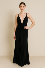 Model wearing a floor-length maxi dress with a plunging neckline, gathered detailing at the waist, and an open crisscross back with tie closure.