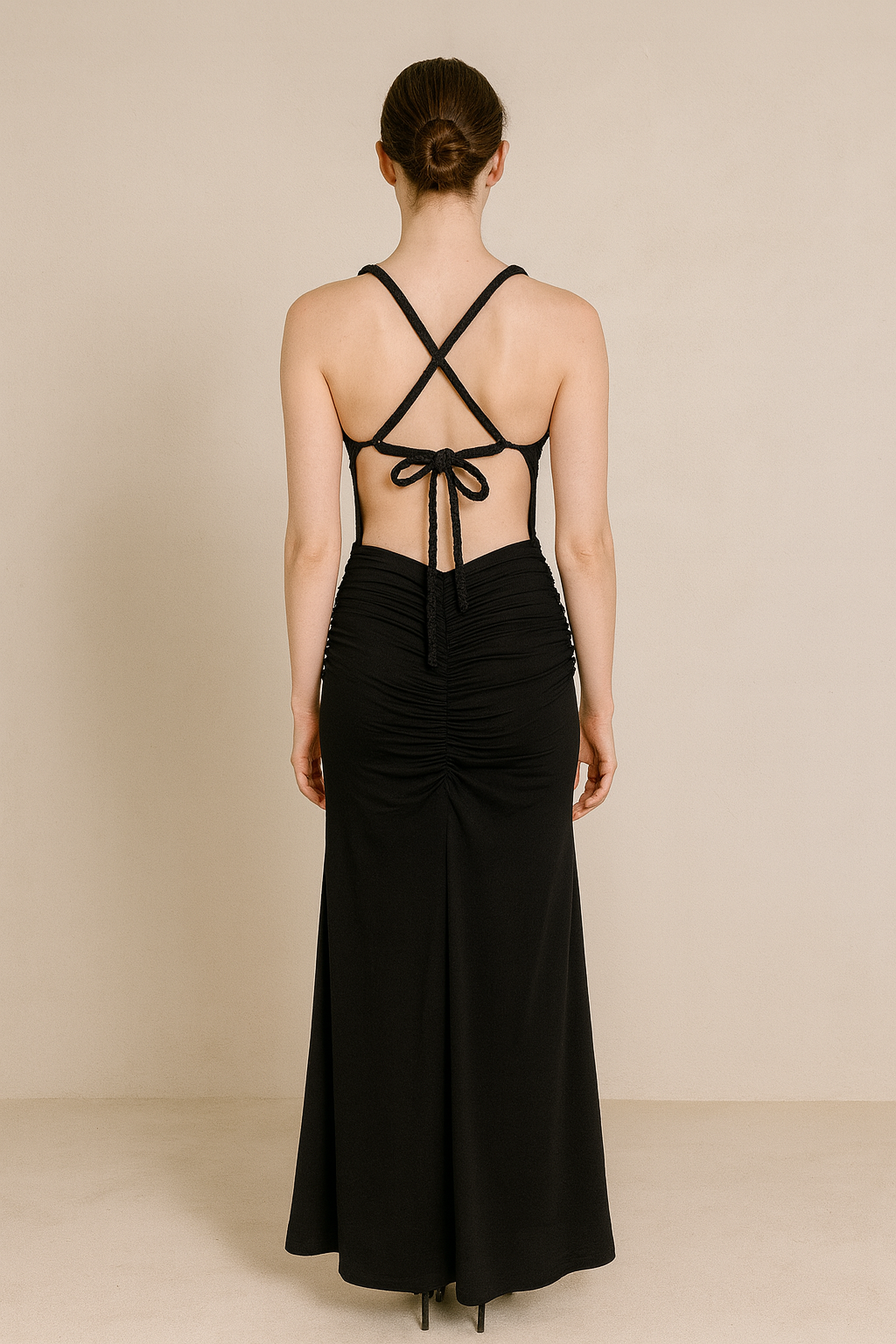 Model wearing a floor-length maxi dress with a plunging neckline, gathered detailing at the waist, and an open crisscross back with tie closure.
