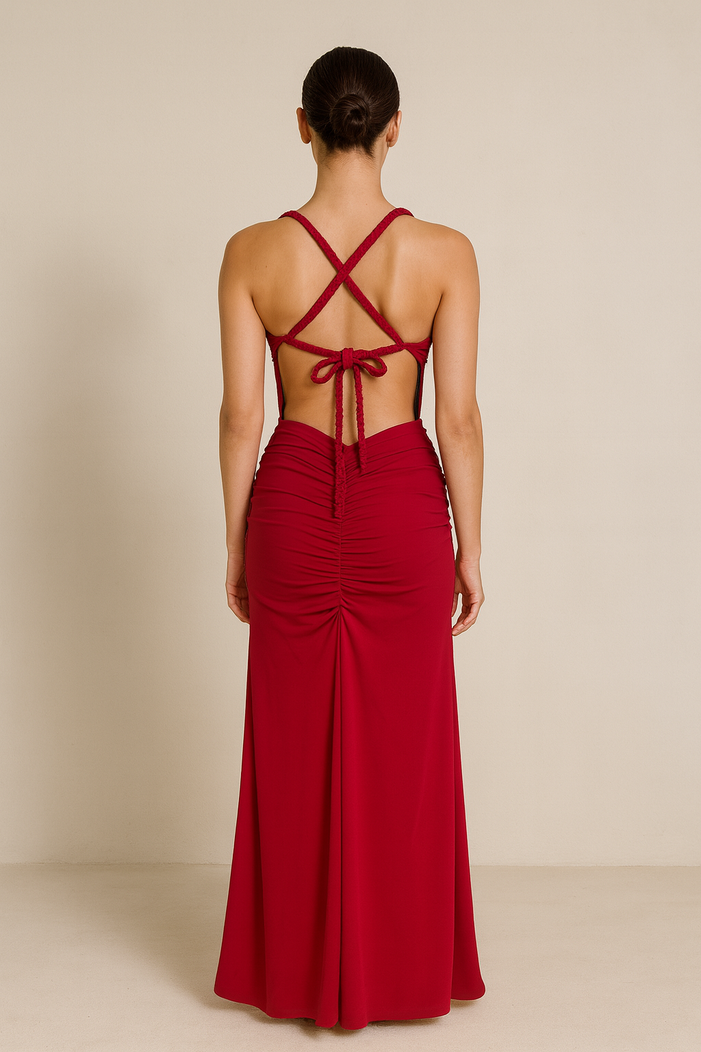 Model wearing a floor-length maxi dress with a plunging neckline, gathered detailing at the waist, and an open crisscross back with tie closure.