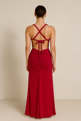 Model wearing a floor-length maxi dress with a plunging neckline, gathered detailing at the waist, and an open crisscross back with tie closure.