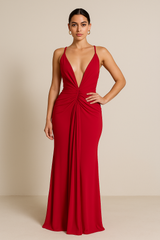 Model wearing a floor-length maxi dress with a plunging neckline, gathered detailing at the waist, and an open crisscross back with tie closure.