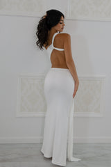Model wearing a white one-shoulder maxi dress featuring a side waist cutout, front tie draping, and floor-length hem