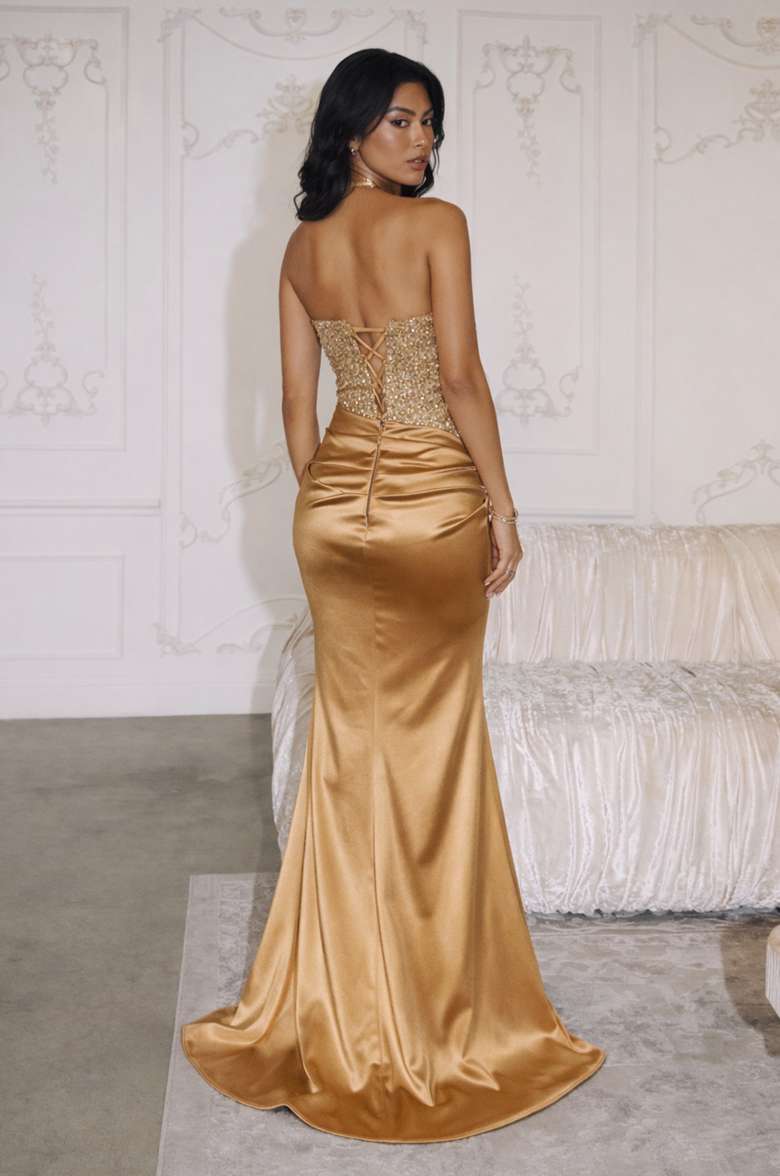 Woman wearing a black strapless gown with a sequin-embellished corset bodice, draped satin skirt, thigh-high slit, and lace-up back.
