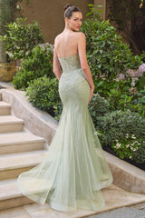 Woman in a strapless green evening gown standing on steps with greenery in the background