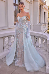 A model stands on an outdoor balcony wearing a strapless off-the-shoulder gown in pale icy blue and champagne with intricate floral embroidery, long white gloves, and a long matching blue train.