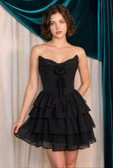 Woman wearing a black strapless dress with ruffled layers against a teal curtain background