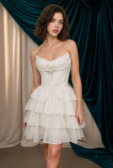 Woman wearing a white strapless dress with ruffled layers against a draped curtain background