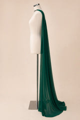 A long, flowing dark green sheer fabric draped over a white dress form mannequin on a metal stand, set against a solid light beige background.