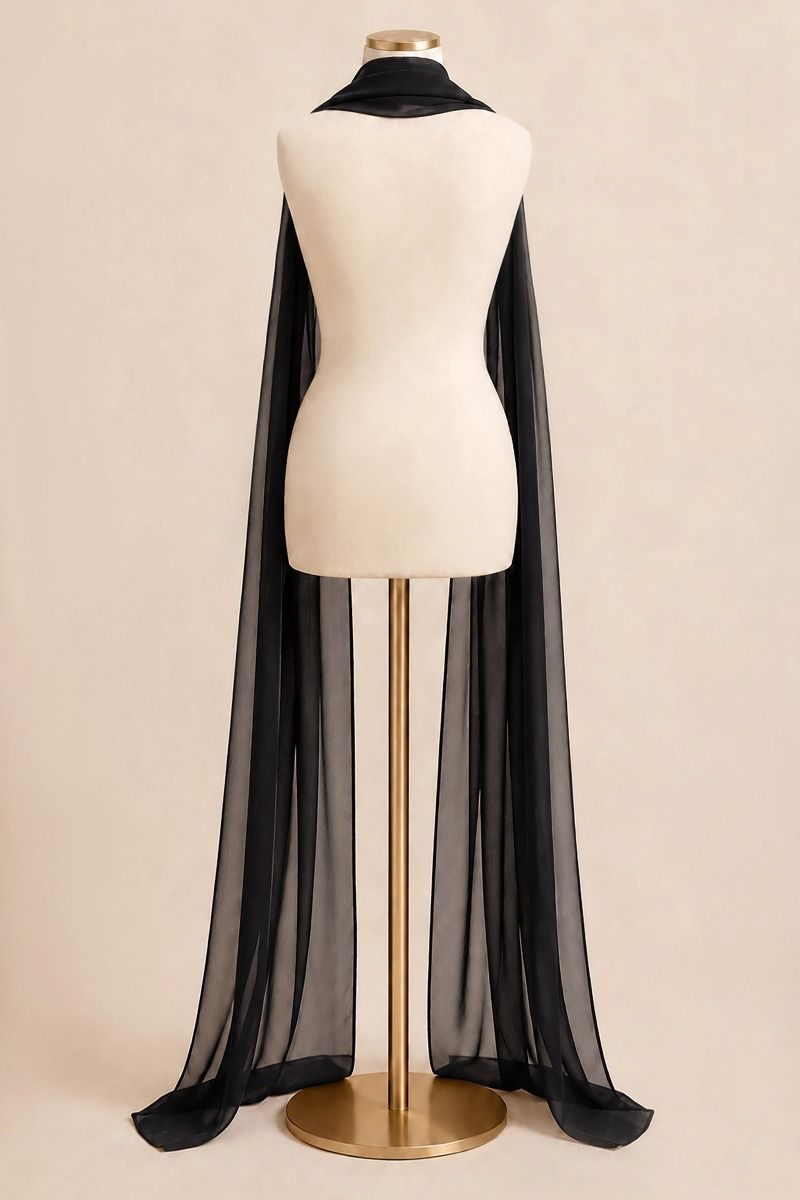 A long sheer black cape draped over a cream dress form mannequin on a gold stand, set against a solid beige background.