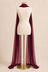 A sheer, lightweight dark burgundy cape or wrap draped over a cream-colored mannequin torso on a gold stand, set against a solid beige background.