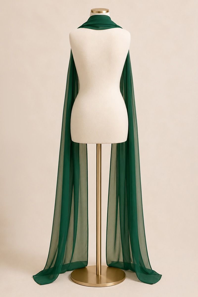 A dark green sheer mesh cape draped over a cream-colored mannequin torso on a gold stand, set against a solid beige background.