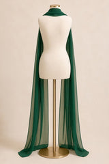 A dark green sheer mesh cape draped over a cream-colored mannequin torso on a gold stand, set against a solid beige background.