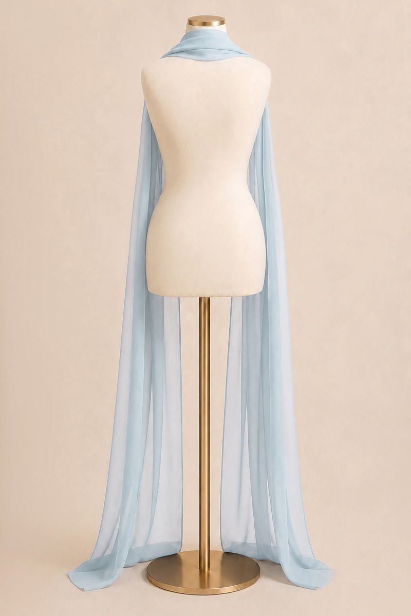 A light blue sheer cape-style scarf draped over a cream mannequin torso on a gold stand, photographed against a plain warm beige studio background.