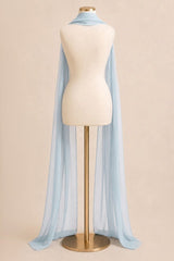 A light blue sheer cape-style scarf draped over a cream mannequin torso on a gold stand, photographed against a plain warm beige studio background.