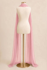 A light pink sheer chiffon cape draped over a cream-colored mannequin torso on a gold stand, set against a solid beige background.