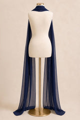 A long sheer navy blue scarf draped over a cream dress form mannequin on a gold stand, set against a solid beige background.