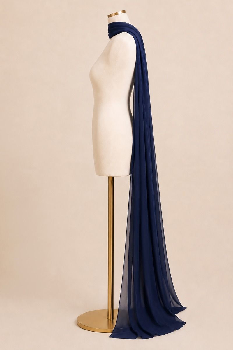 A navy blue sheer chiffon scarf draped over a cream-colored dress form mannequin on a gold stand, set against a solid beige background.