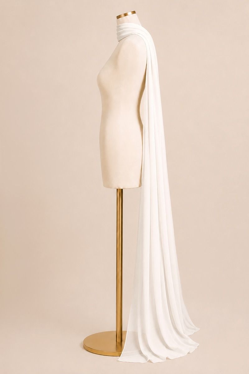A long flowing white bridal veil draped over a cream mannequin torso on a gold stand, photographed against a warm beige studio background.