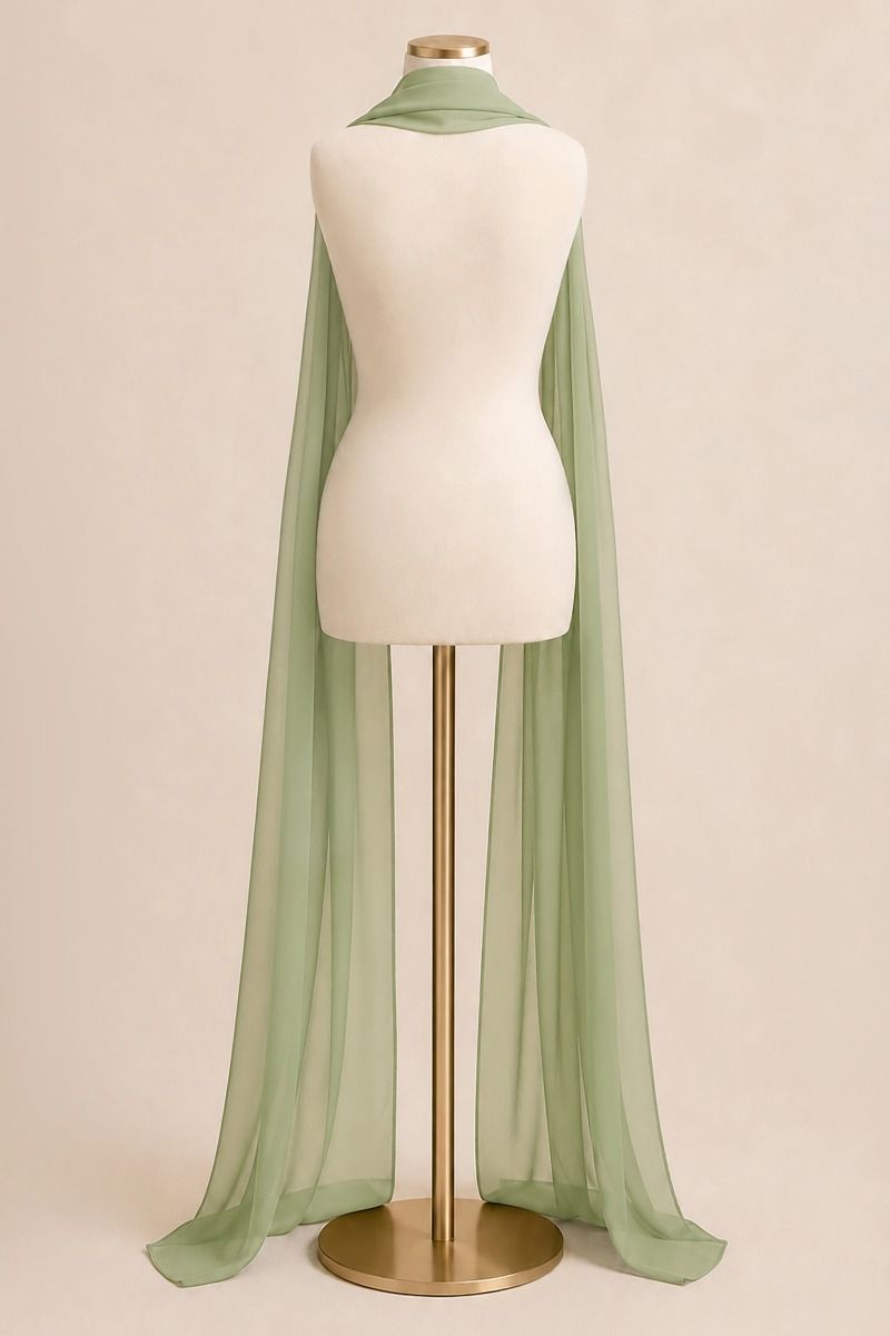 A sage green sheer chiffon cape draped over a cream-colored dress form mannequin on a gold stand, set against a solid warm beige background.