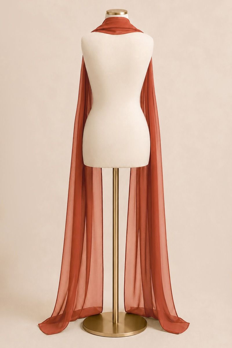 A rust-orange sheer cape scarf draped over a cream-colored mannequin torso on a gold stand, set against a solid beige background.