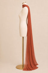 A long, semi-sheer rust-colored scarf draped over a cream dress form mannequin on a gold stand, set against a solid beige background.
