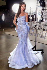 Woman in a sparkling evening gown standing next to a chandelier in a glamorous setting.