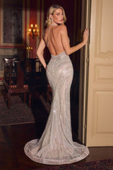 A woman models a sparkling silver backless mermaid gown in an elegant indoor room with warm lighting and a cream door behind her.