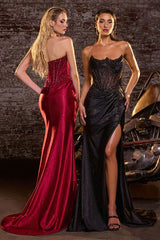 Two women in elegant evening gowns standing next to a vintage car with a rustic wall background.