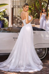 Woman in a white wedding dress standing next to a vintage car with another woman in a white dress in the background.