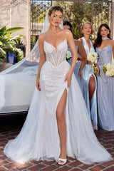 Woman in a white wedding dress with a high slit, standing outdoors with other women in light blue dresses.