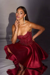 Woman wearing a burgundy strapless gown with a high slit on a dark background