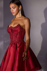 Woman wearing a red strapless gown with beaded details against a gray background