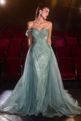 A woman models a strapless off-the-shoulder evening gown in a dimly lit theater with rows of red seats. The gown is a light mint green with shimmering sequined details and a flowing tulle skirt.