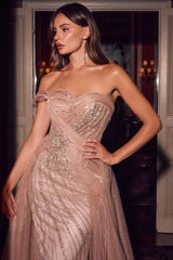 A woman modeling a strapless champagne pink evening gown with intricate beaded detailing and a sheer tulle skirt, posed in front of a dark doorway.