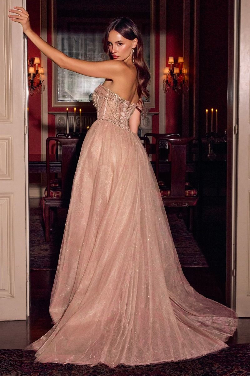 A woman wearing a strapless dusty pink tulle ball gown with a fitted embellished bodice and a full flowing skirt, posed in a dimly lit, elegant room with candles.