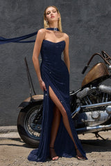 A woman models a sparkling navy blue strapless gown with a high thigh slit, standing next to a vintage motorcycle against a dark textured wall.