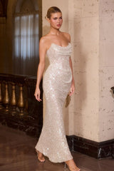 Woman in a sparkling evening gown standing in an elegant interior setting.