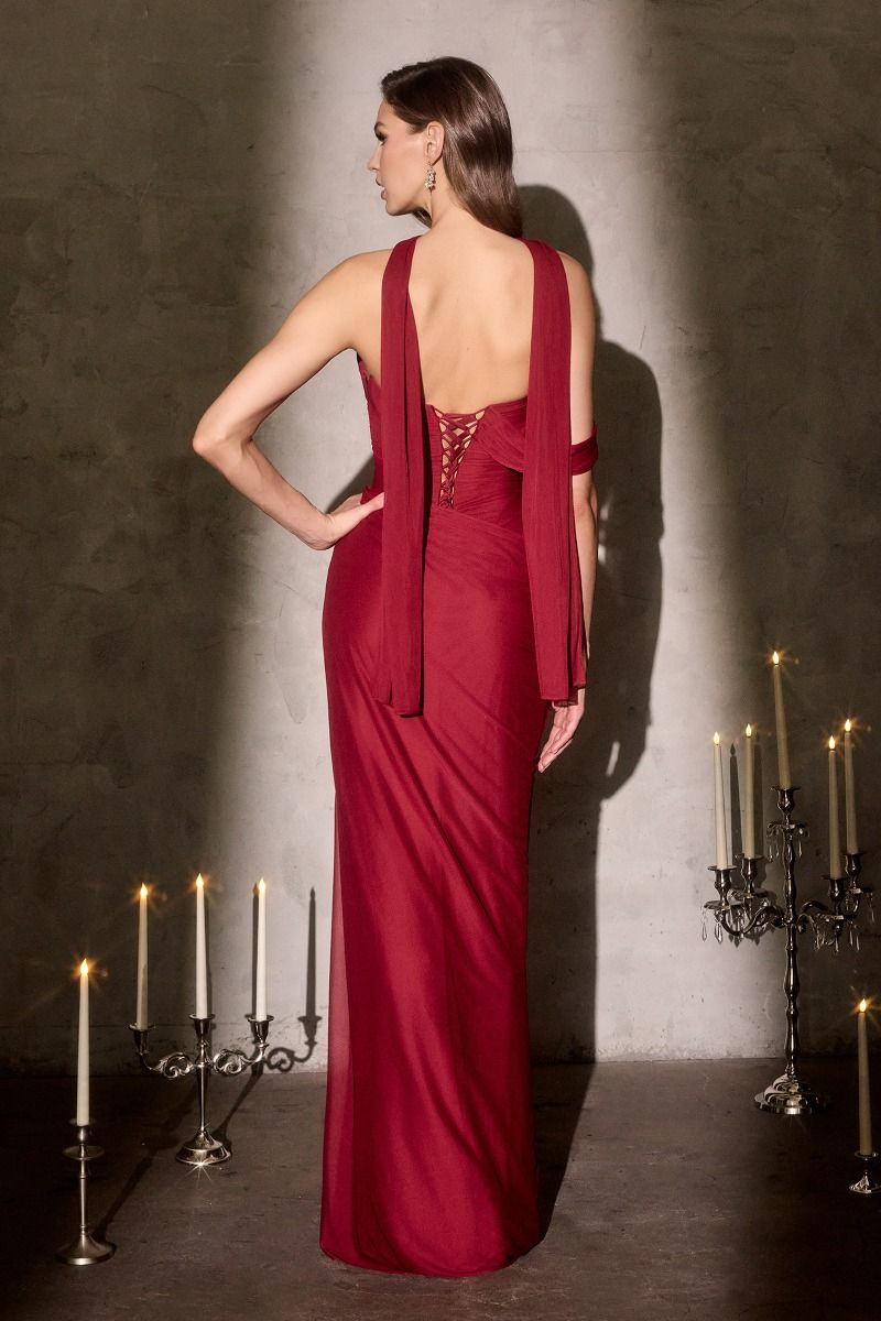 Woman in a red evening gown standing in a dimly lit room with candles.