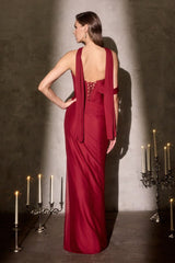 Woman in a red evening gown standing in a dimly lit room with candles.