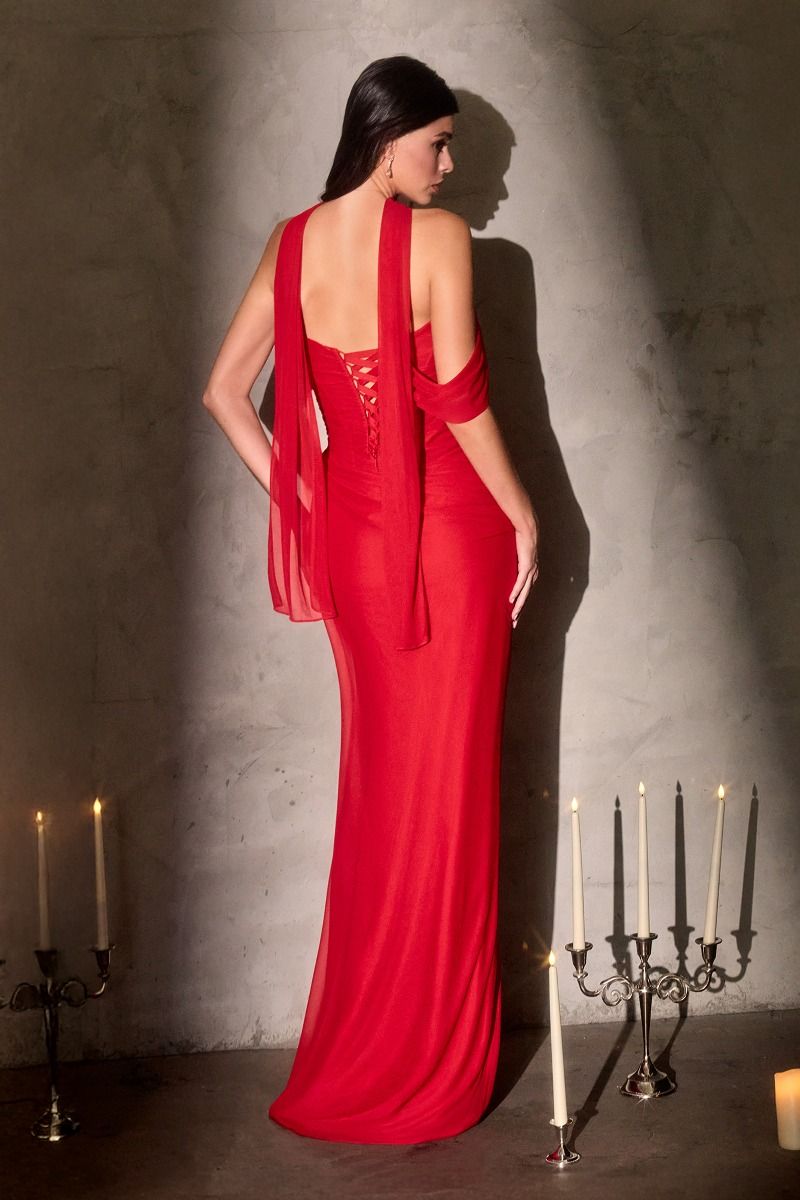 Woman in a red evening gown standing against a textured wall with candles.